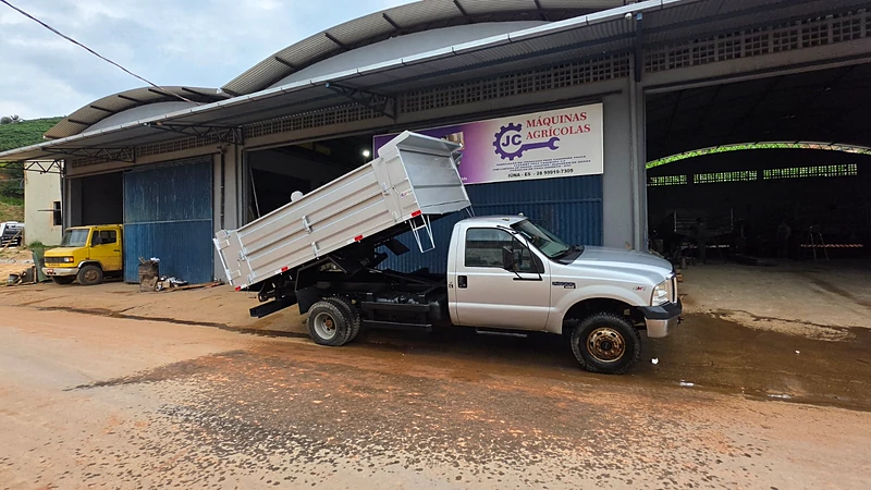 Caçamba branca erguida em teste de basculamento, em frente à JC