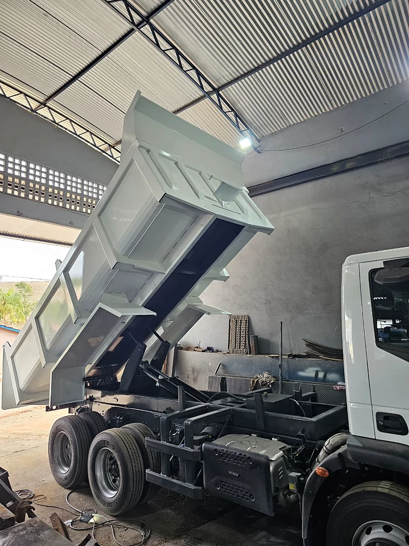 Caçamba fechada de cor clara, erguida em posição de descarga dentro do galpão