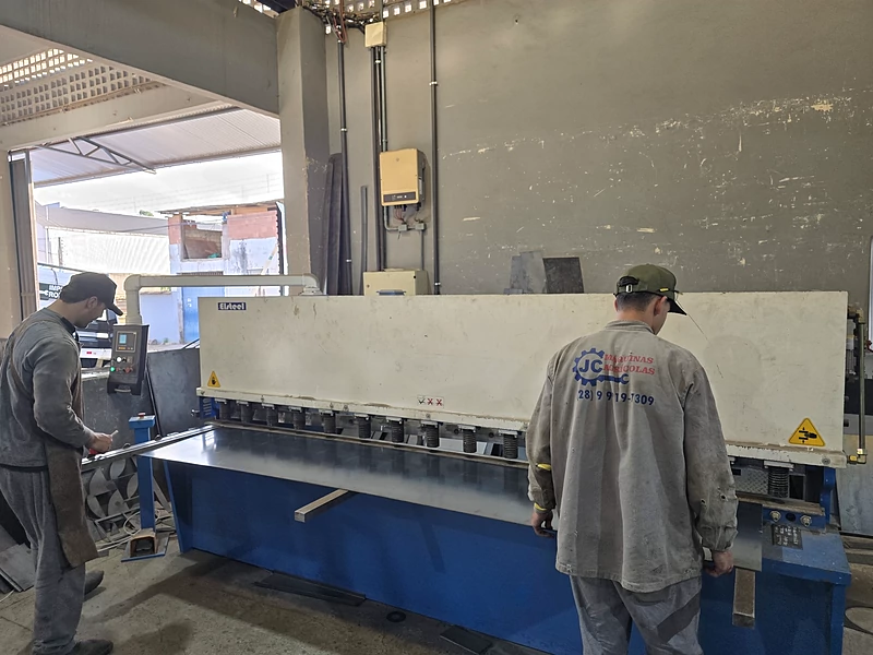 Dois profissionais da JC operando a guilhotina no galpão