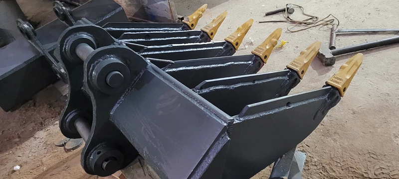 Ancinho preto visto de lado, com as unhas amarelas em fila, no chão da fábrica da JC